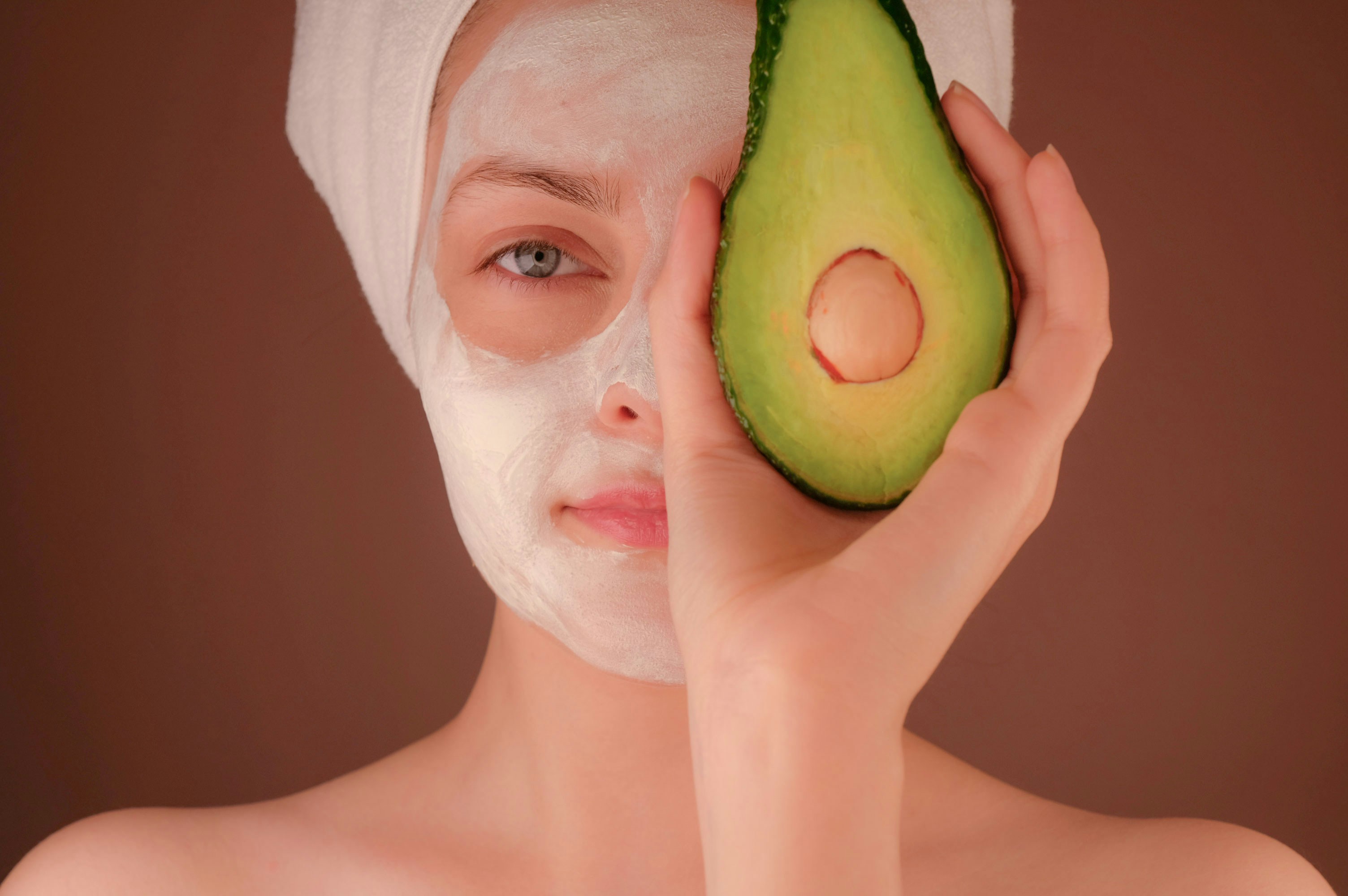 Woman in spa towel holding an avocado half to her face