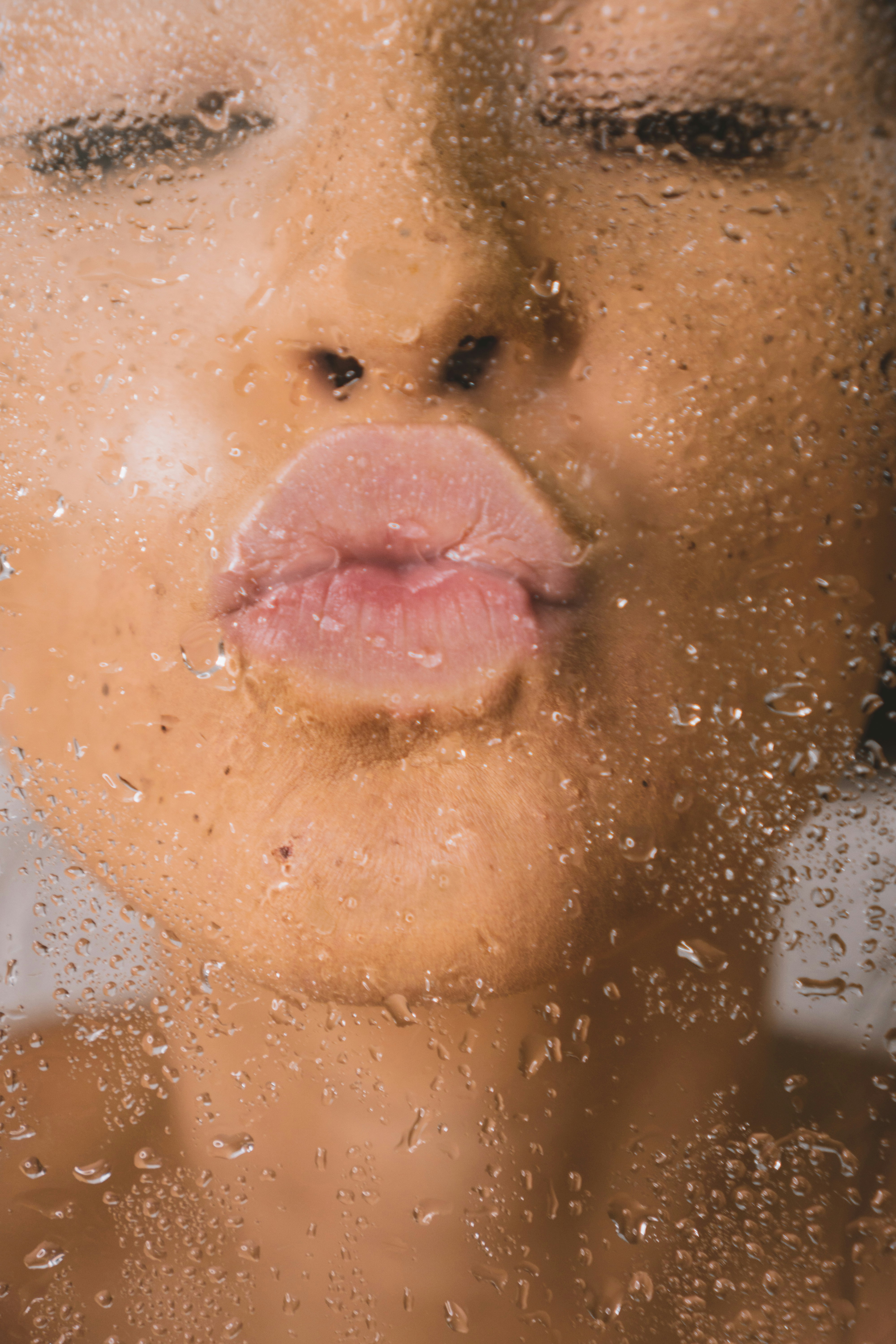 Close-up of a woman's face through water droplets on glass
